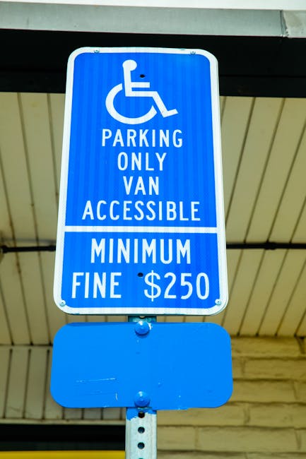 A blue parking restriction sign indicating designated parking for accessible vans only, featuring an icon of a person in a wheelchair, with the message 'Parking Only Van Accessible' and a minimum fine of $250. The sign is mounted on a metal pole beneath a canopy or shelter, with a wooden or laminated ceiling visible above. The sign is located outdoors in an area where house removals, furniture transport, or loading processes may occur, especially suggesting regulations relevant during home relocation or moving logistics managed by Man With a Van Barnsbury. The environment appears to be an urban or commercial setting, with the sign designed to ensure proper parking for vehicles involved in moving and relocation services.
